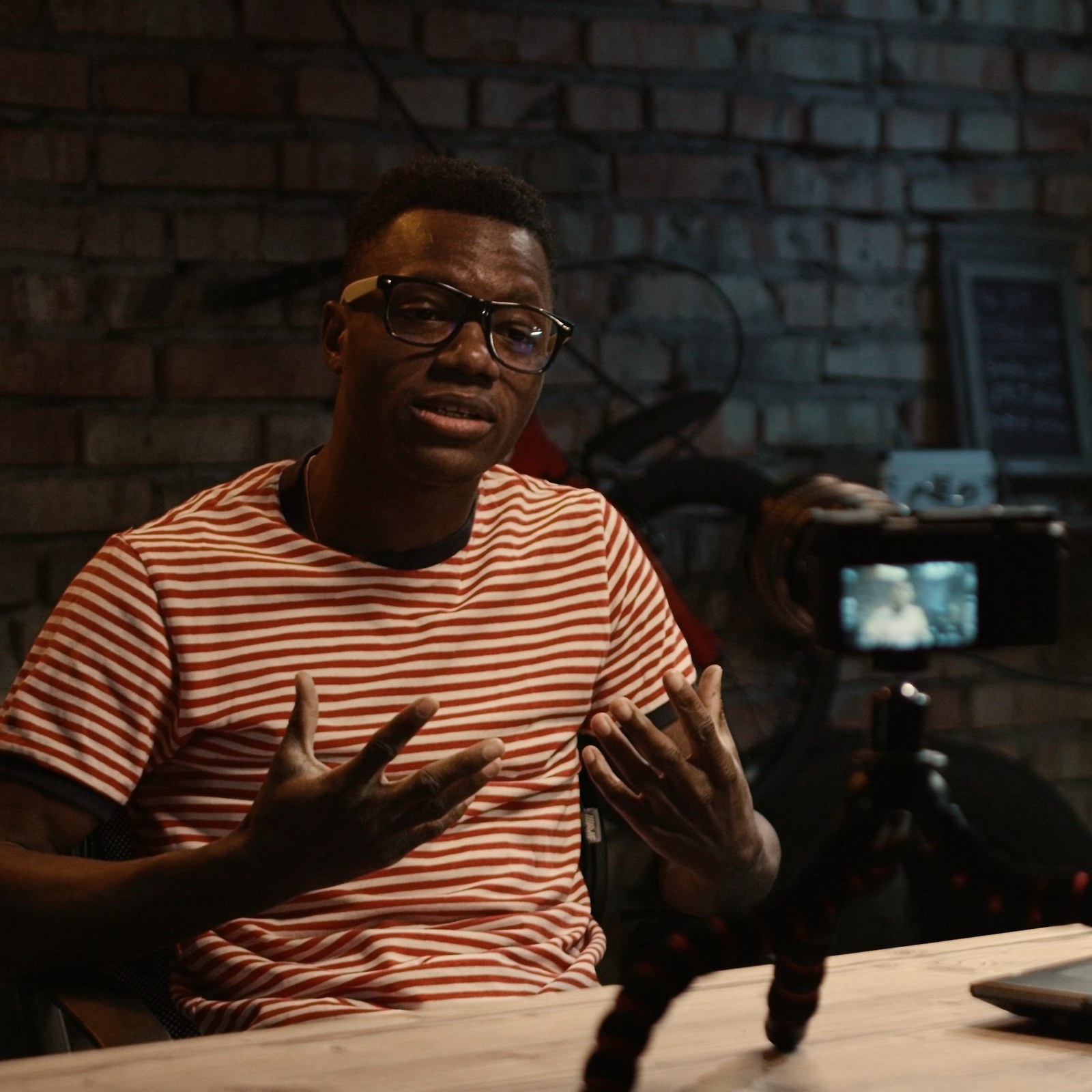 A creator studio lit by a warm practical lamp, camera on a tripod, screens glowing in the background.